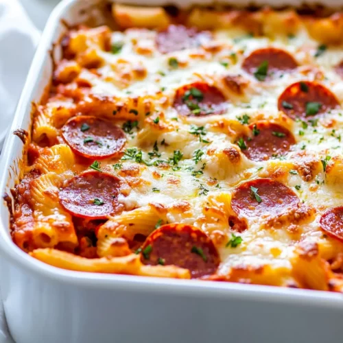 Baked Pizza Pasta Recipe - A Cheesy, Family-Friendly Dinner 3 Baked Pizza Pasta In A White Dish Topped With Golden Melted Cheese, Crispy Pepperoni, And Fresh Parsley, Served With A Spoon.