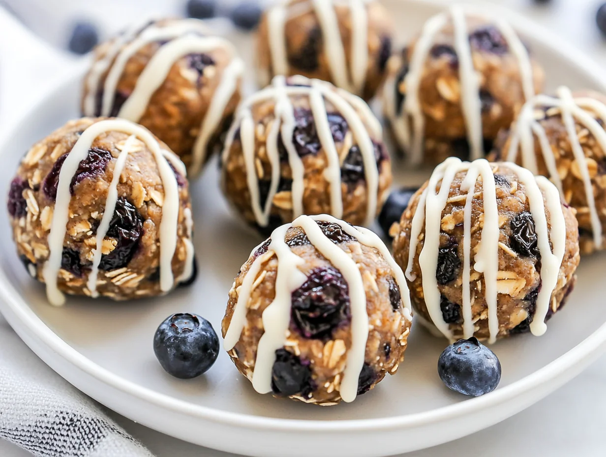 Blueberry Energy Balls On A White Plate, Drizzled With Melted White Chocolate And Topped With Chopped Blueberries.