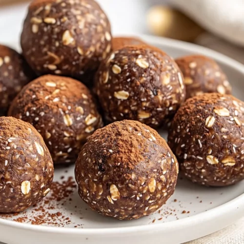 Close-Up Of Chocolate Protein Balls On A White Plate, Garnished With Cocoa Powder And Chocolate Shavings, Light Gray Napkin Nearby