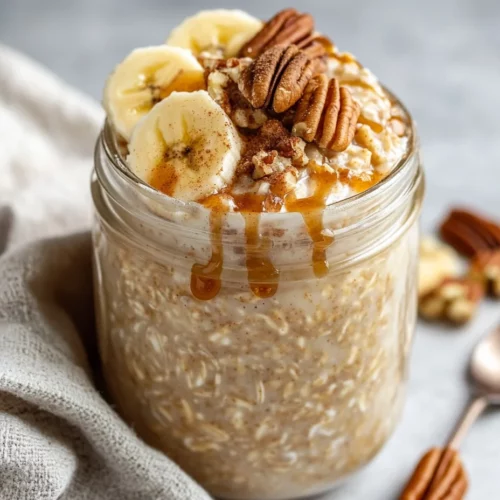 Cinnamon Roll Overnight Oats In A Glass Jar Topped With Banana Slices And Pecans, Drizzled With Brown Sugar.