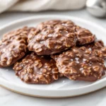 Stack Of Glossy Chocolate Classic No-Bake Cookies On A White Plate With Parchment Paper, Garnished With Coarse Sea Salt.