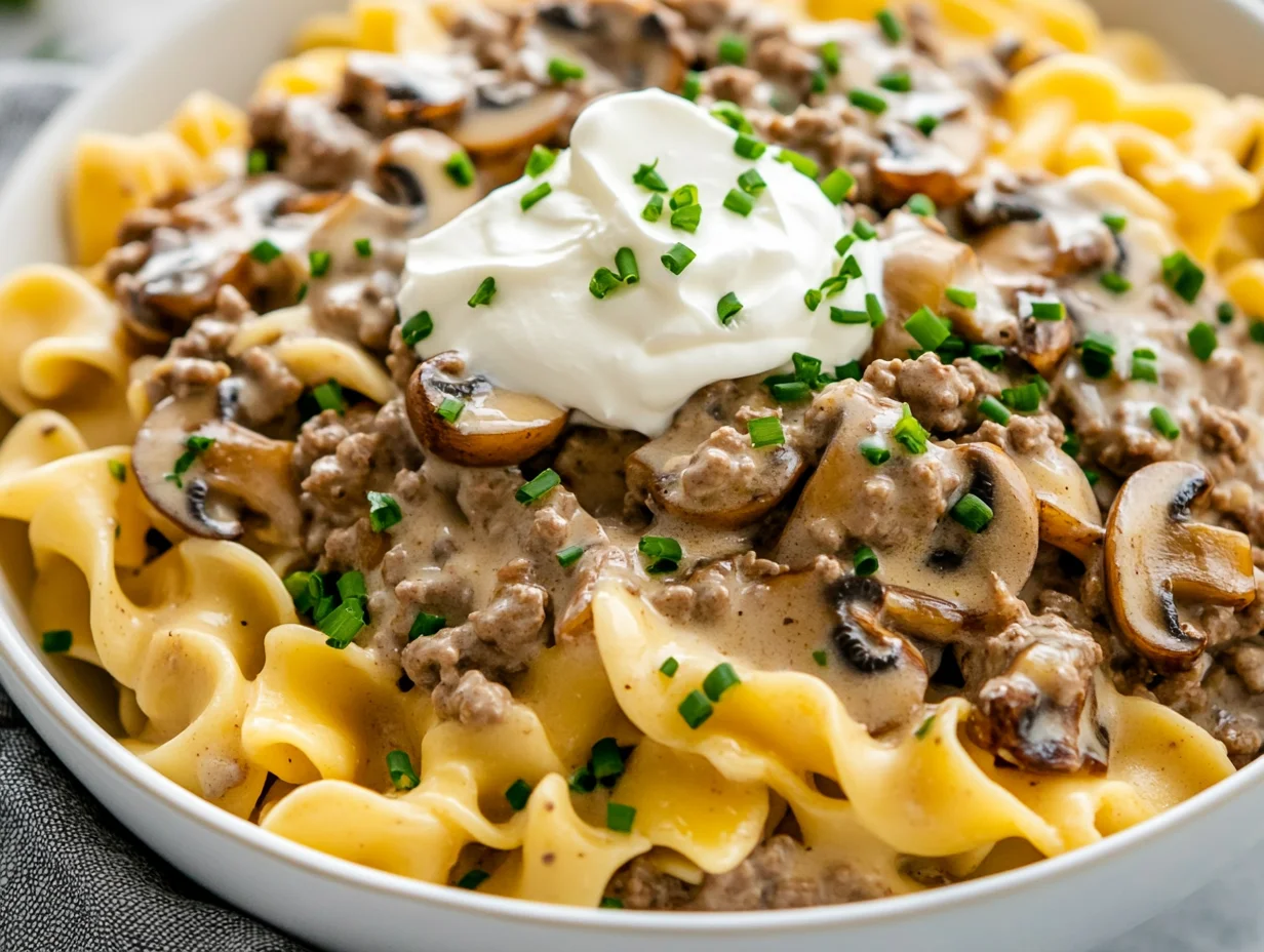 Bowl Of Ground Beef Stroganoff Noodles Topped With Sour Cream And Fresh Chives, Warm And Inviting On A White Background.
