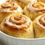Freshly Baked Homemade Orange Sweet Rolls In A White Dish Drizzled With Citrus Icing And Garnished With Bright Orange Zest.