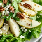 Roquefort Pear Salad Served On A White Plate, Topped With Candied Pecans And Fresh Parsley