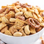 Crunchy Snack Mix For Game Day In A White Bowl With Caramel-Coated Cereal, Pretzels, And Peanuts