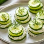 Platter Of Cucumber Party Sandwiches Topped With Fresh Dill On A White Plate, Showcasing Playful Shapes.