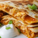 Crispy Buffalo Chicken Quesadilla Wedges On A White Plate Topped With Sour Cream And Green Onions