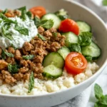 A Colorful Low-Carb Turkey Gyro Bowl With Seasoned Turkey, Tzatziki, Cucumbers, And Cherry Tomatoes On A White Plate