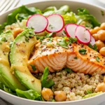 Salmon Caesar Salad Bowl With Flaked Salmon, Quinoa, Avocado, And Radish On A White Plate With Caesar Dressing